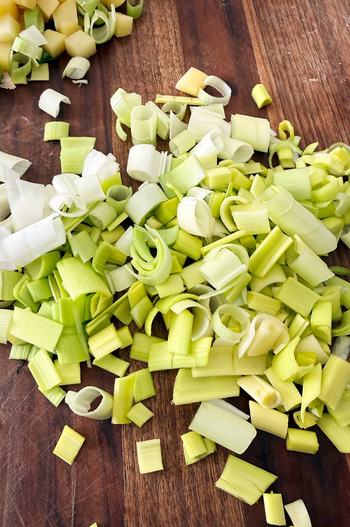 Chopped leeks and diced potatoes on a wooden cutting board.