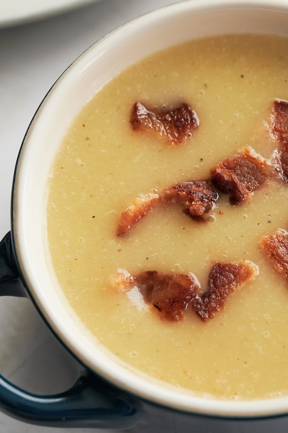 A bowl of creamy bacon potato leek soup topped with several pieces of crispy bacon.