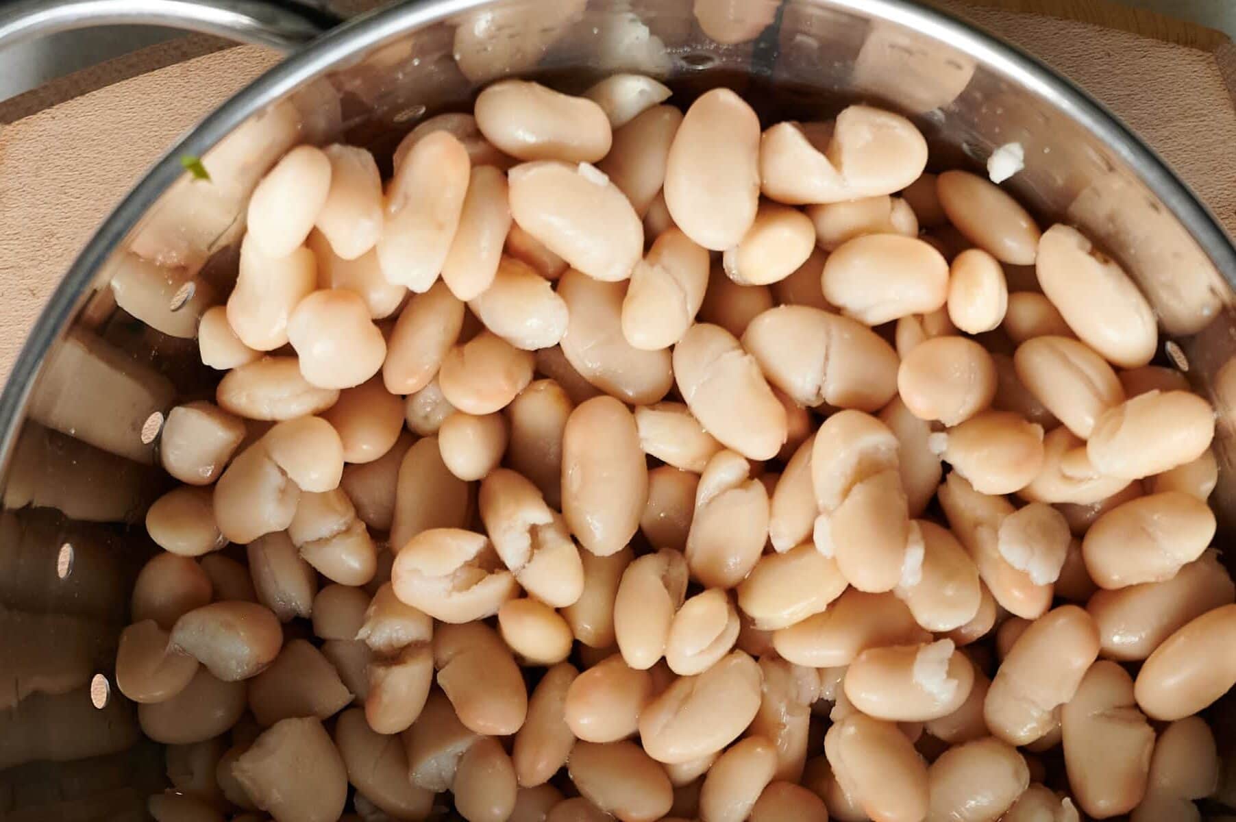 A close-up view of cooked white beans in a stainless steel pot.