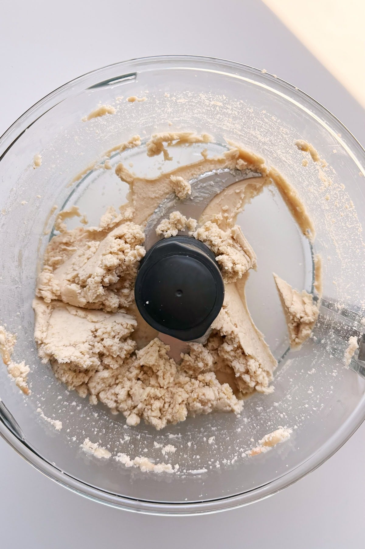 A food processor bowl containing partially mixed cannellini beans with clumps sticking to the sides and base.