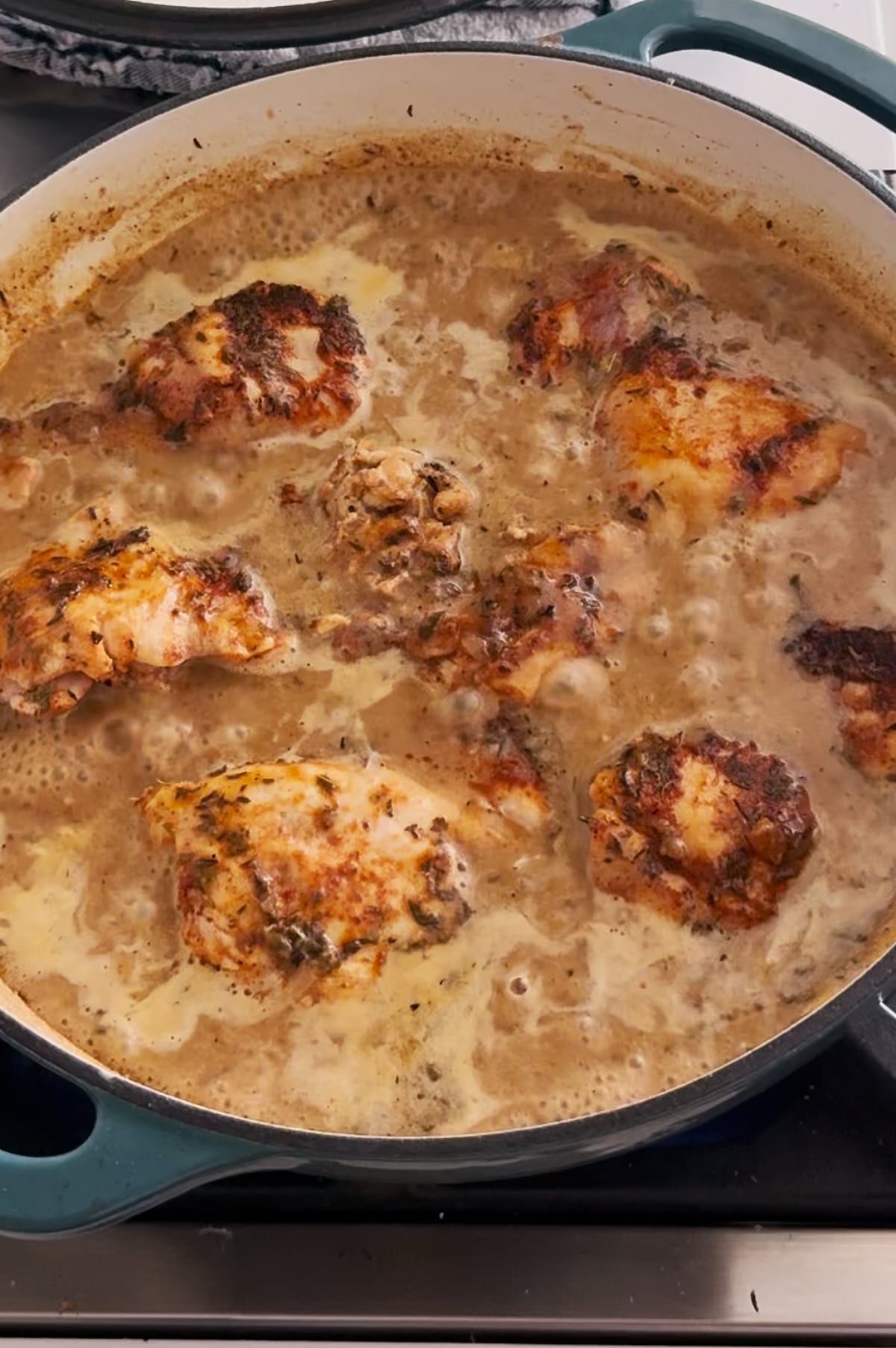 Chicken thighs simmer in a creamy, lemon garlic seasoned sauce inside a large round pot on a stovetop.