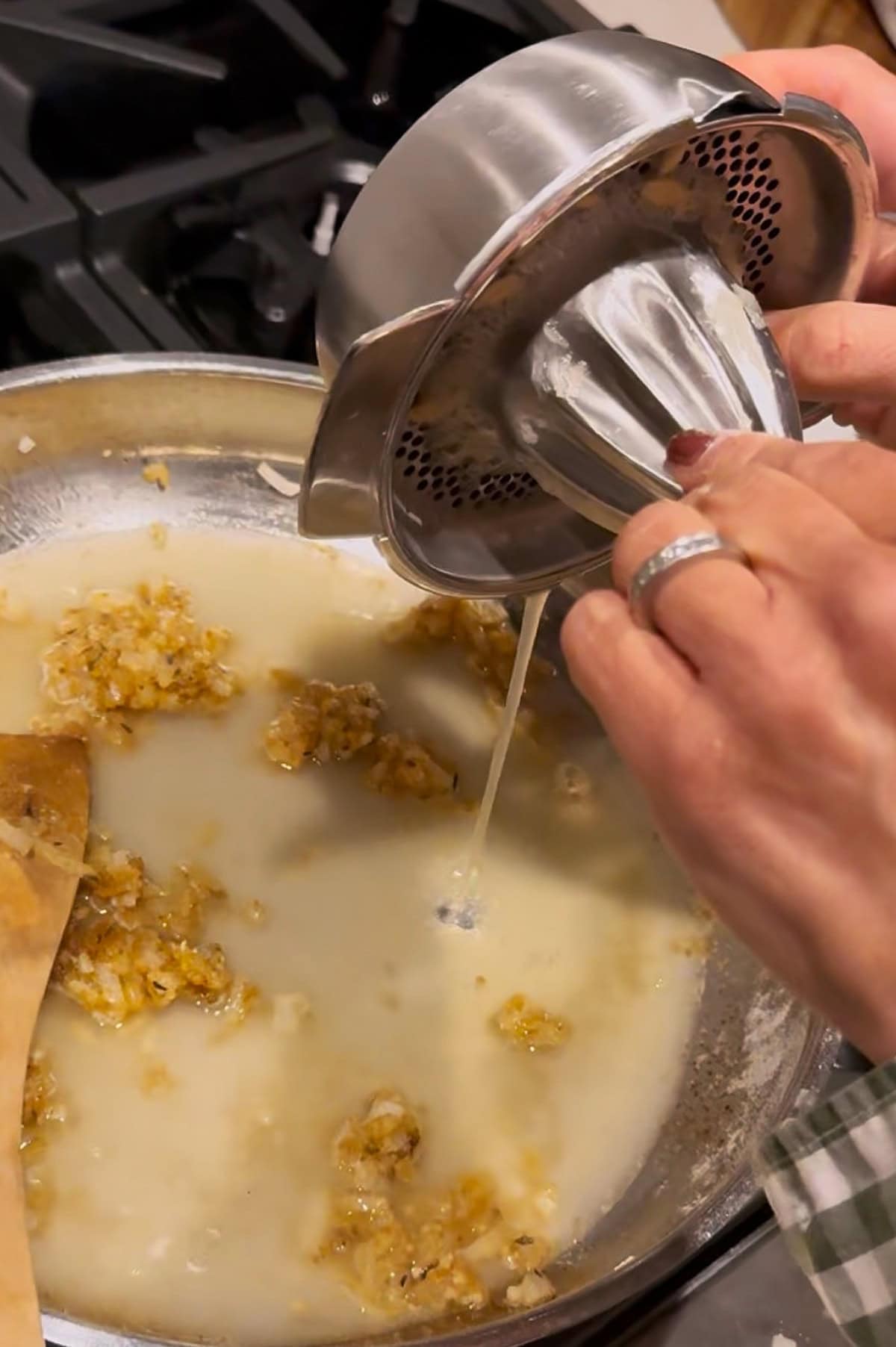 A person squeezes fresh lemon juice into a pan of sautéed garlic sauce on a stovetop.