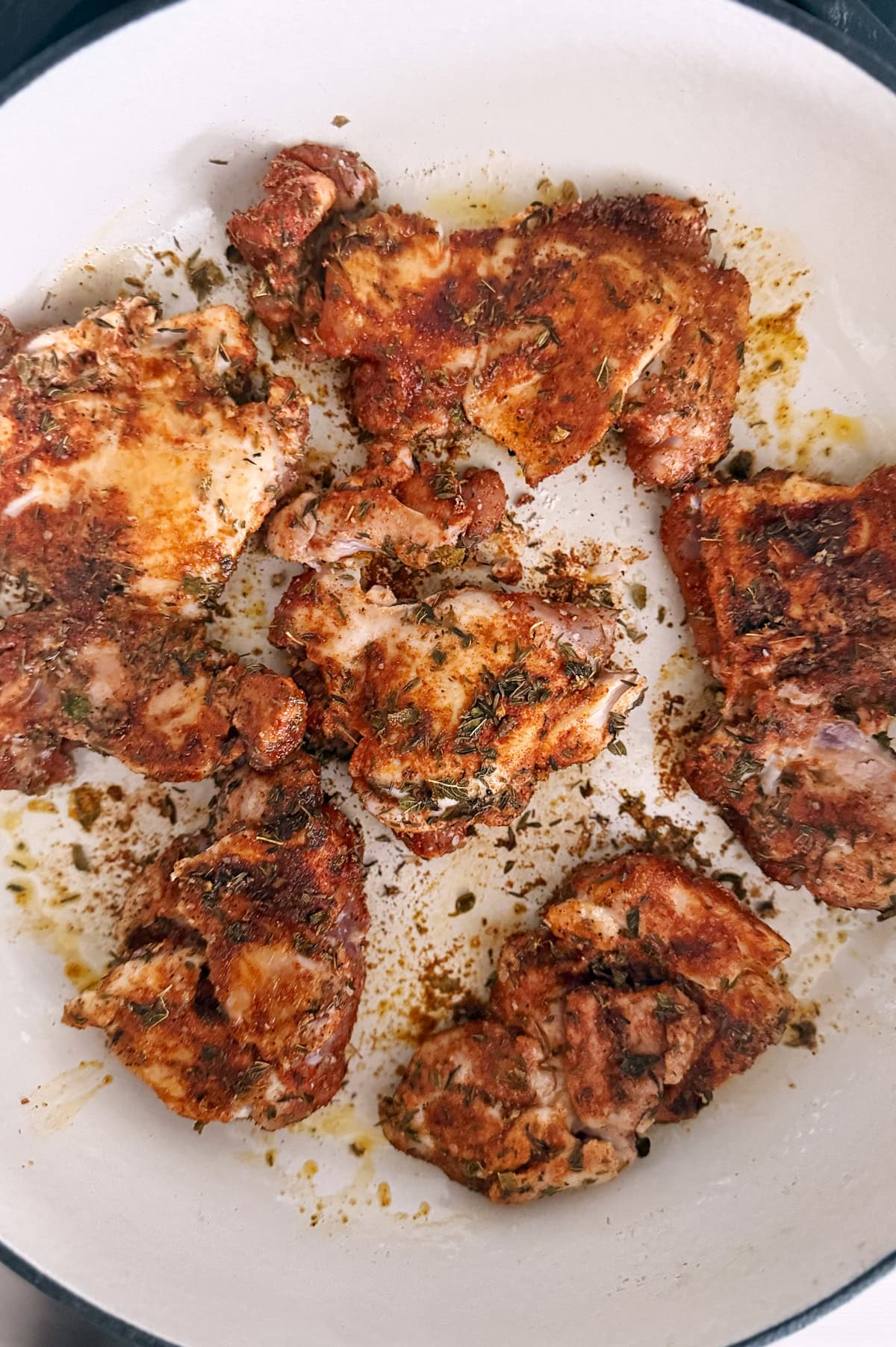 Browned seasoned chicken thighs are arranged in a white skillet.