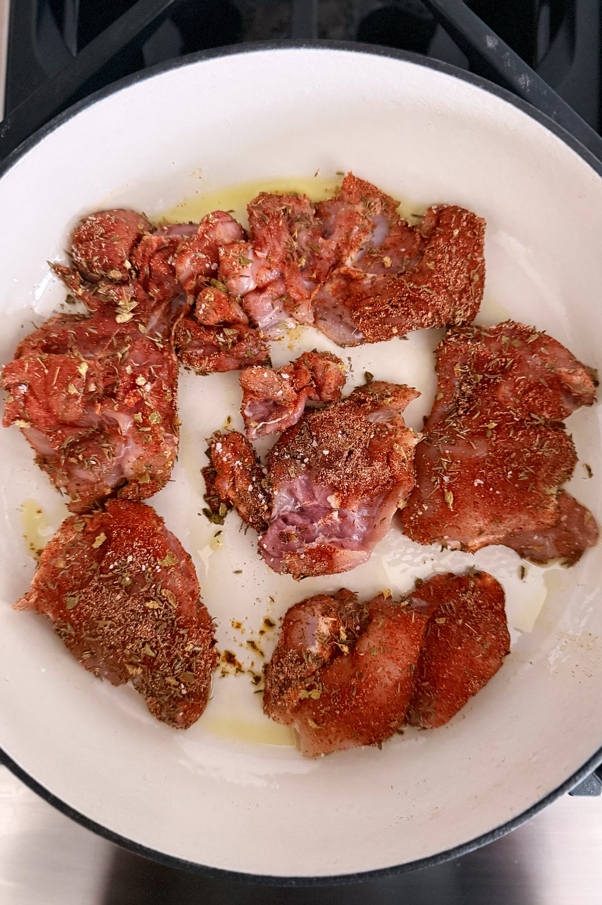 Seasoned chicken thighs browning in a white skillet in small amount of oil.