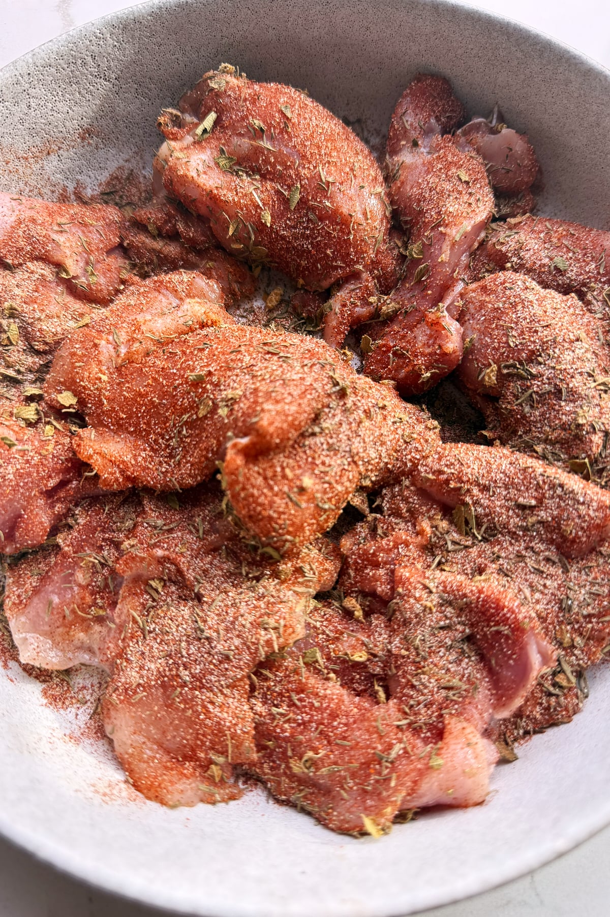 Raw chicken thights in a bowl, coated with a blend of dry herbs and spices, ready for browning.