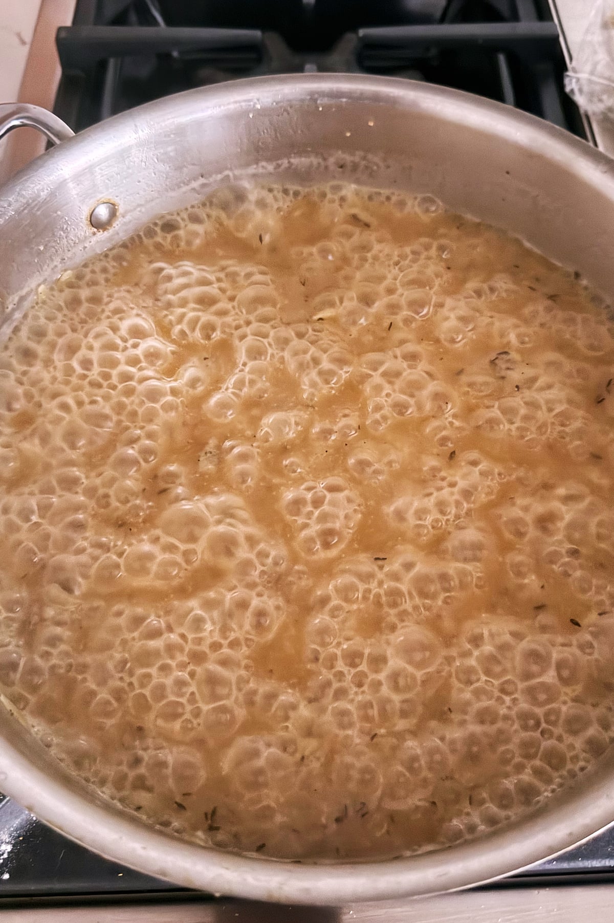 A stainless skillet filled with broth is simmering orzo to cook.