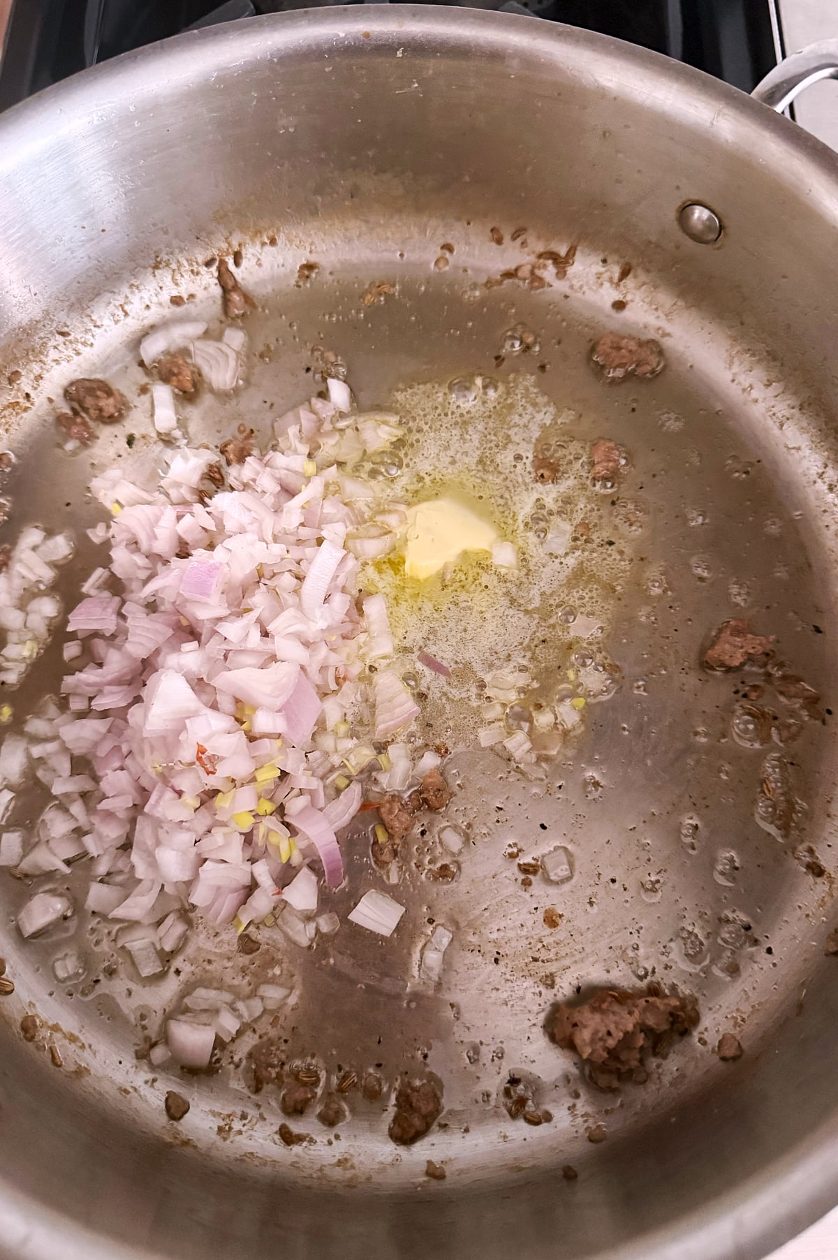 Chopped shallots and a pat of butter sautéing in a stainless steel pan with browned bits from previous cooking.