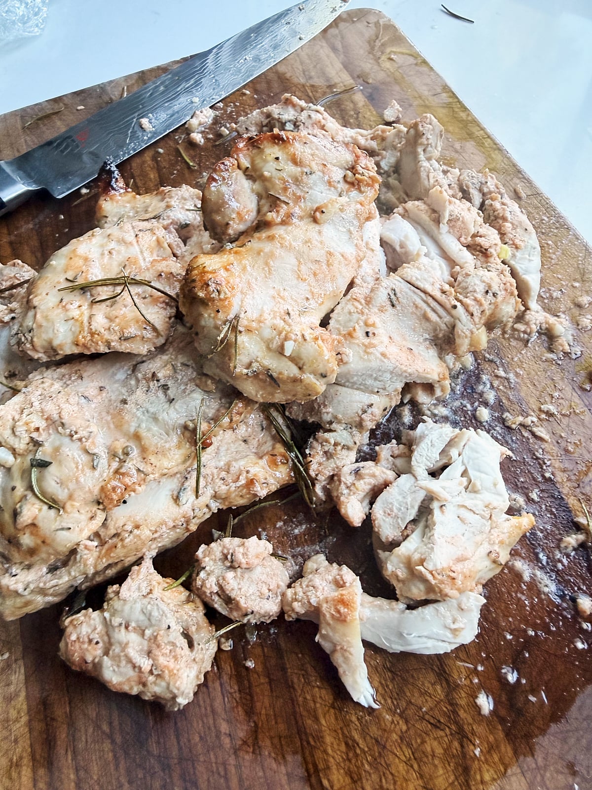 Cooked Italian chicken thighs sliced and piled on a wooden cutting board, with a knife placed nearby. Some seasoning and juices are visible on the meat and board.