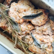 Baked chicken thighs in a roasting pan, seasoned with herbs including sage and rosemary.