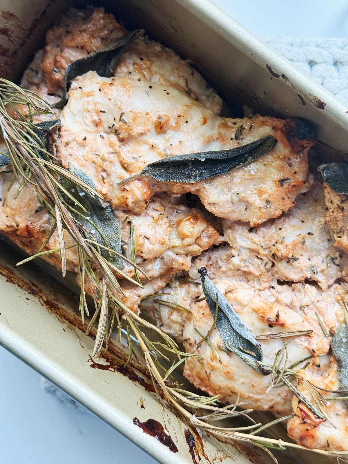 Baked chicken thighs in a roasting pan, seasoned with herbs including sage and rosemary.
