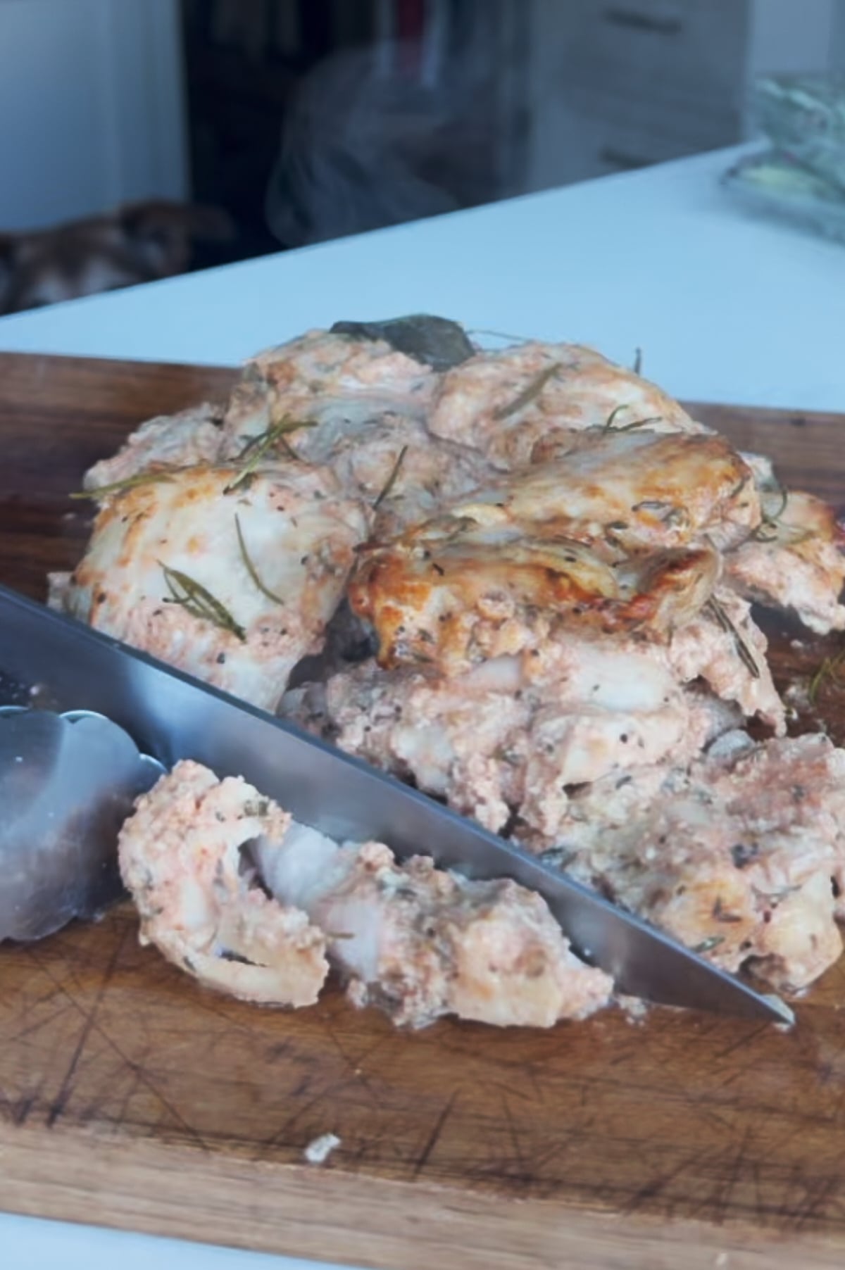 Italian loaf pan chicken pieces being sliced with a large knife on a wooden cutting board.
