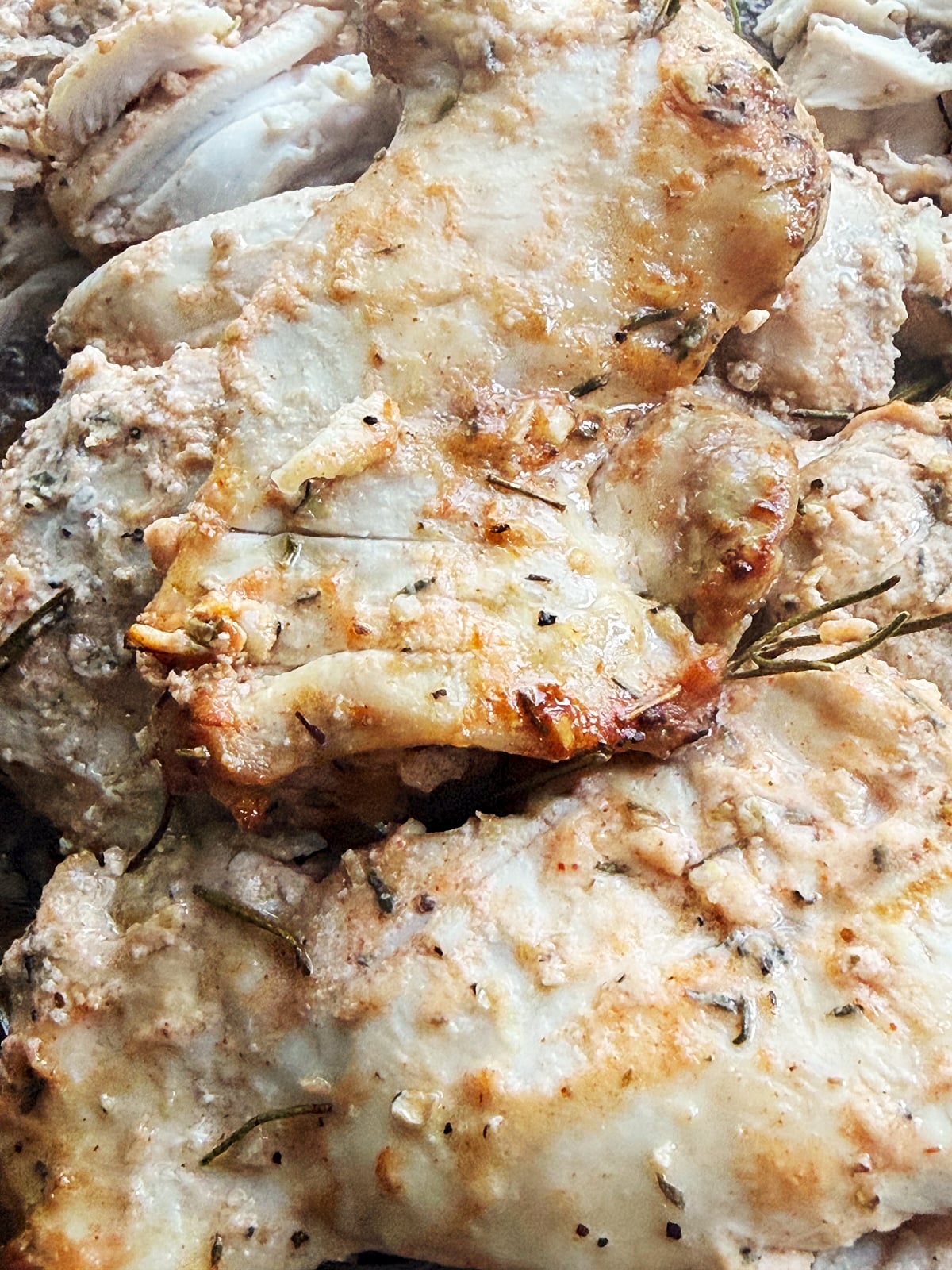 Close-up of cooked, seasoned chicken thighs with visible herbs and browned, grilled surfaces.