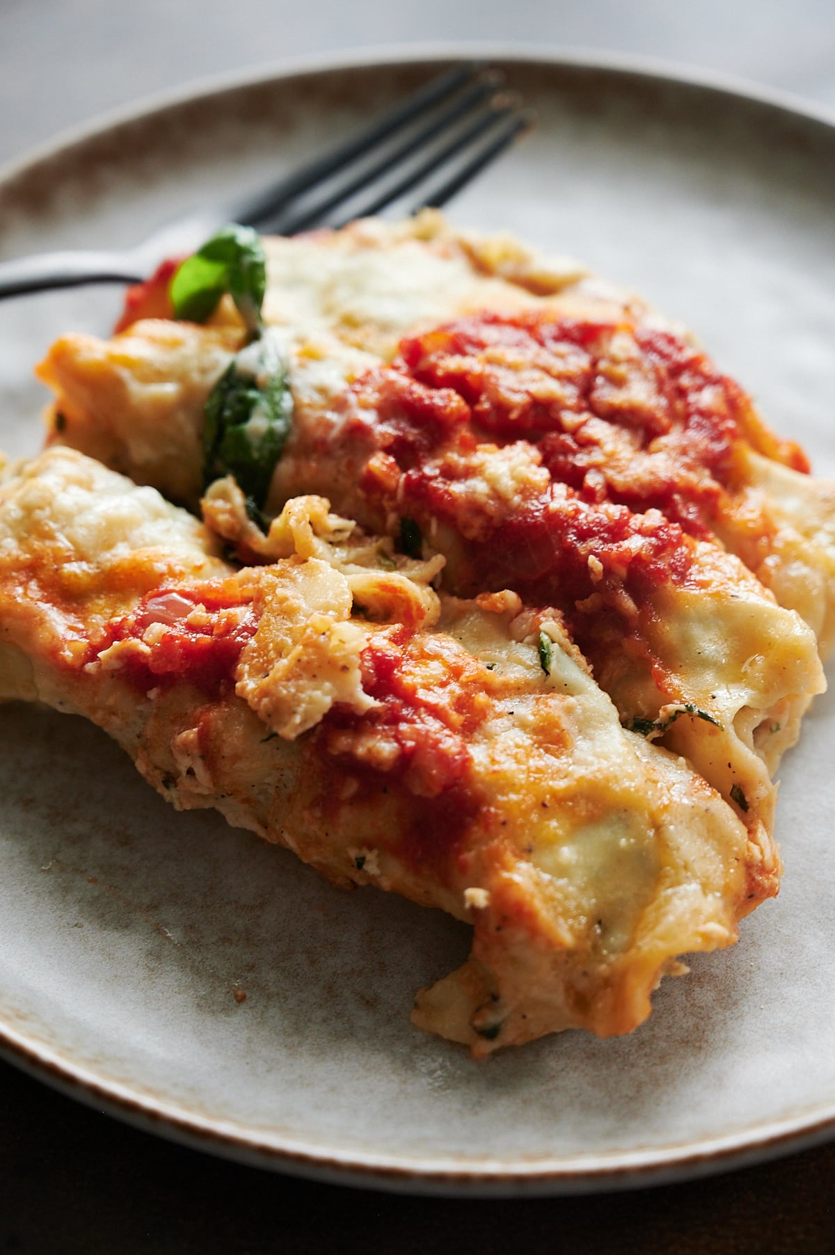 Three cheese-stuffed cannelloni topped with tomato sauce and melted cheese on a plate with a fork in the background.
