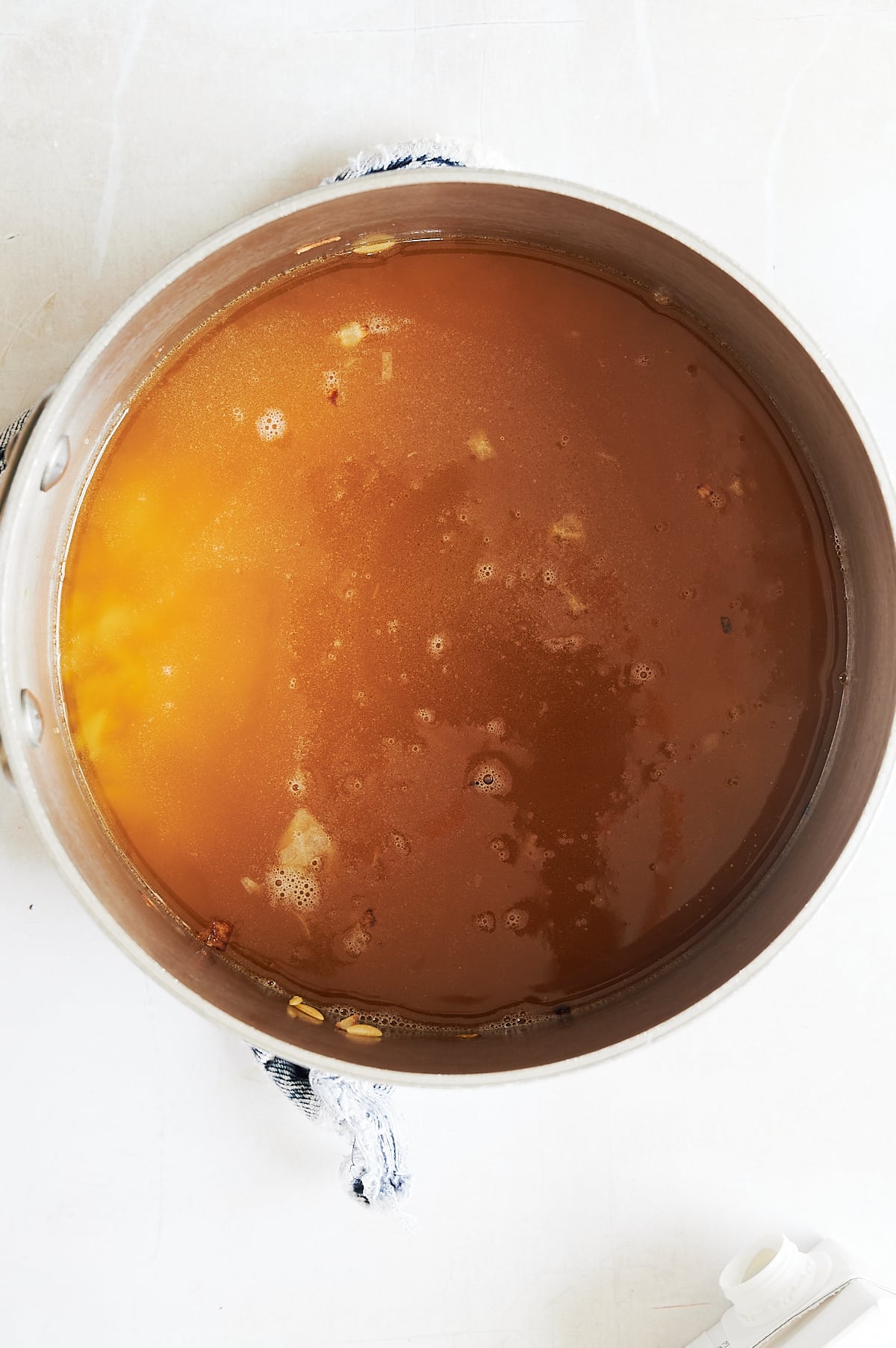 A metal saucepan containing orzo simmering in chicken broth, viewed from directly above.
