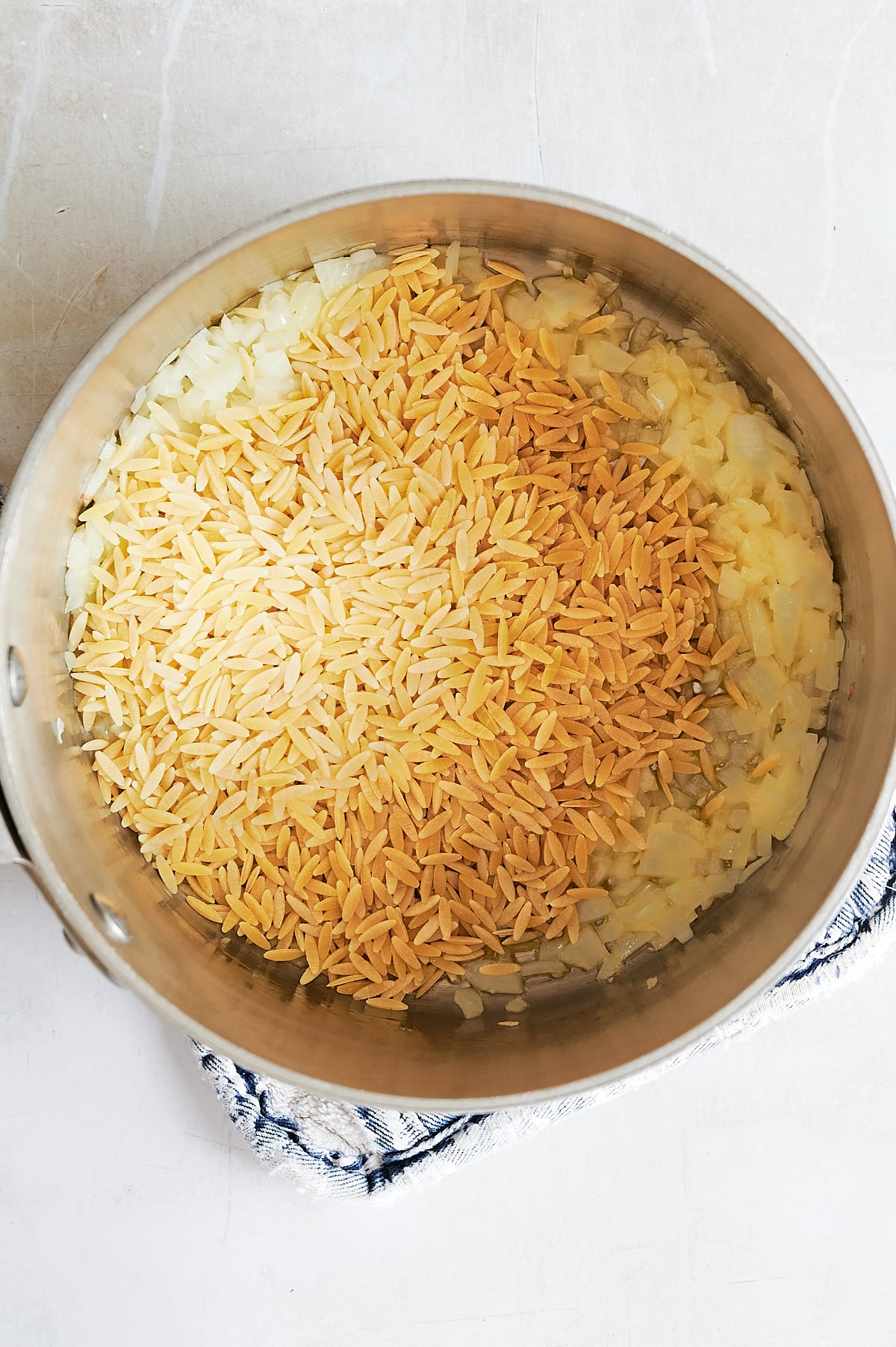 Orzo pasta and chopped onions toasting and sautéing in a metal saucepan.