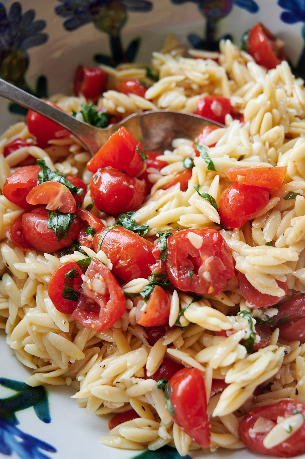 A bowl of orzo pasta salad mixed with halved cherry tomatoes, garlic and fresh basil, served with a spoon.